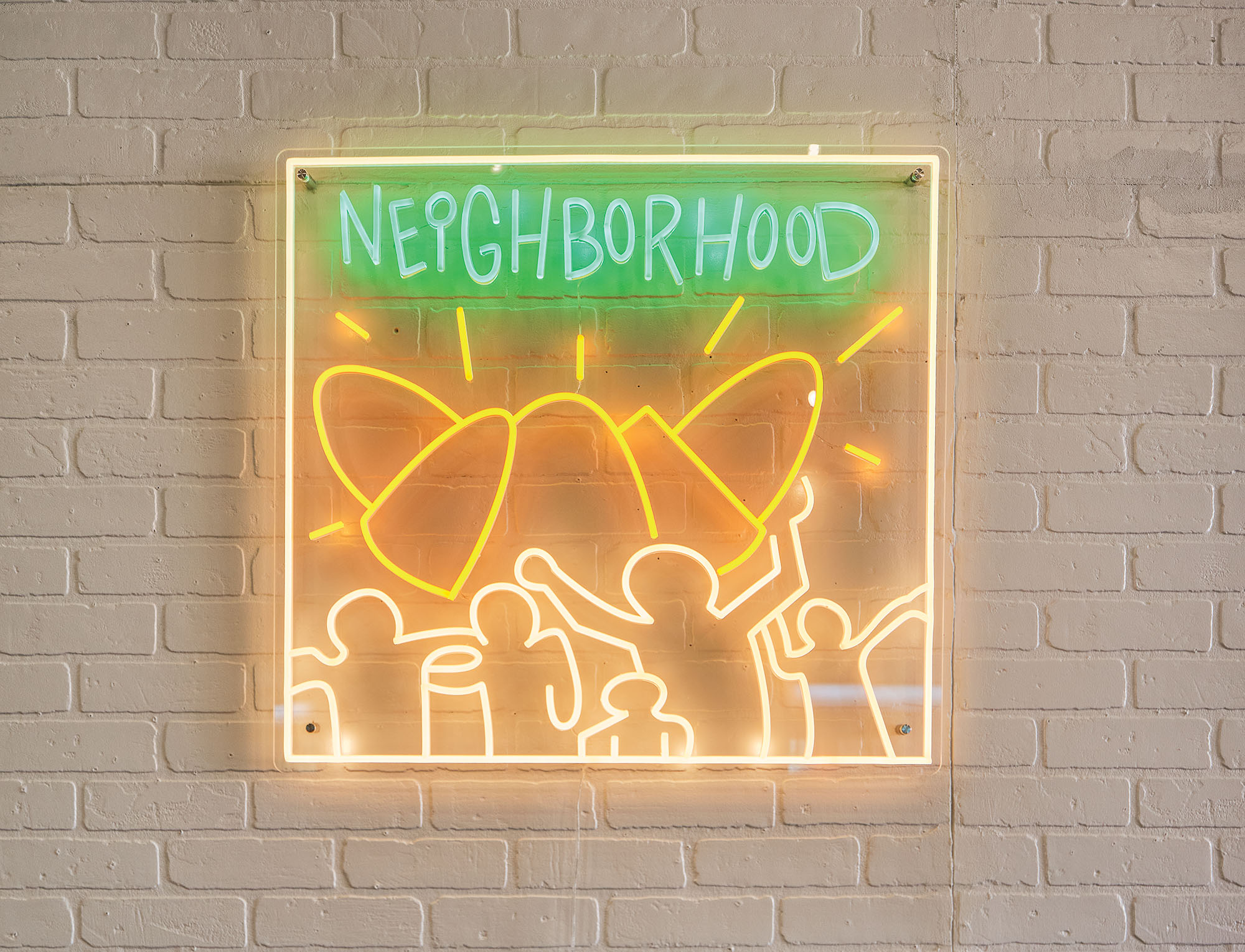 A neon sign on a white brick background, the sign reads 'Neighborhood' with a yellow neon croissant