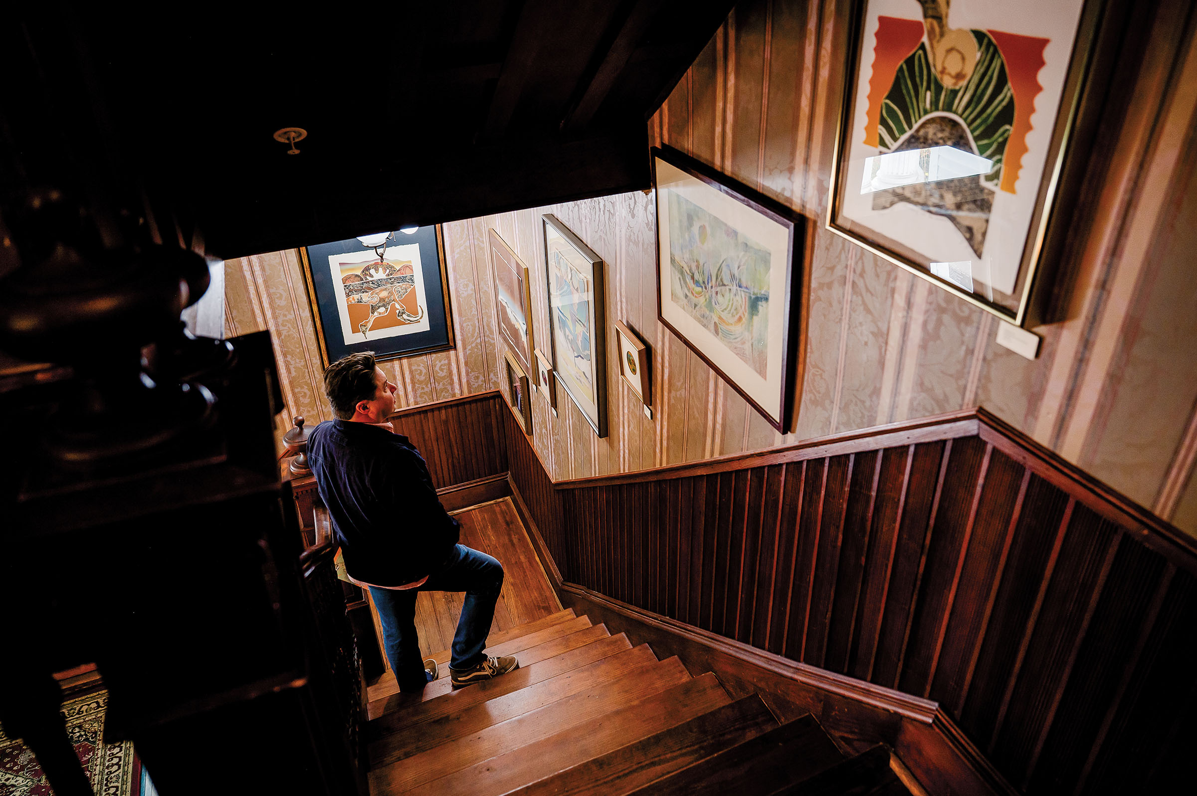 A person walks down a wood-paneled staircase with photographs framed on a wall