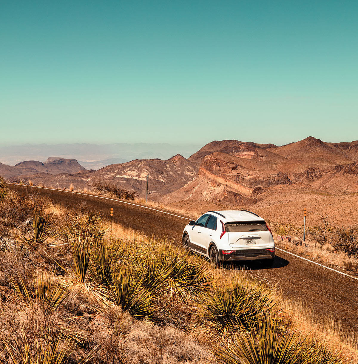A white car drives along a desert landscape underneath a wide blue sky
