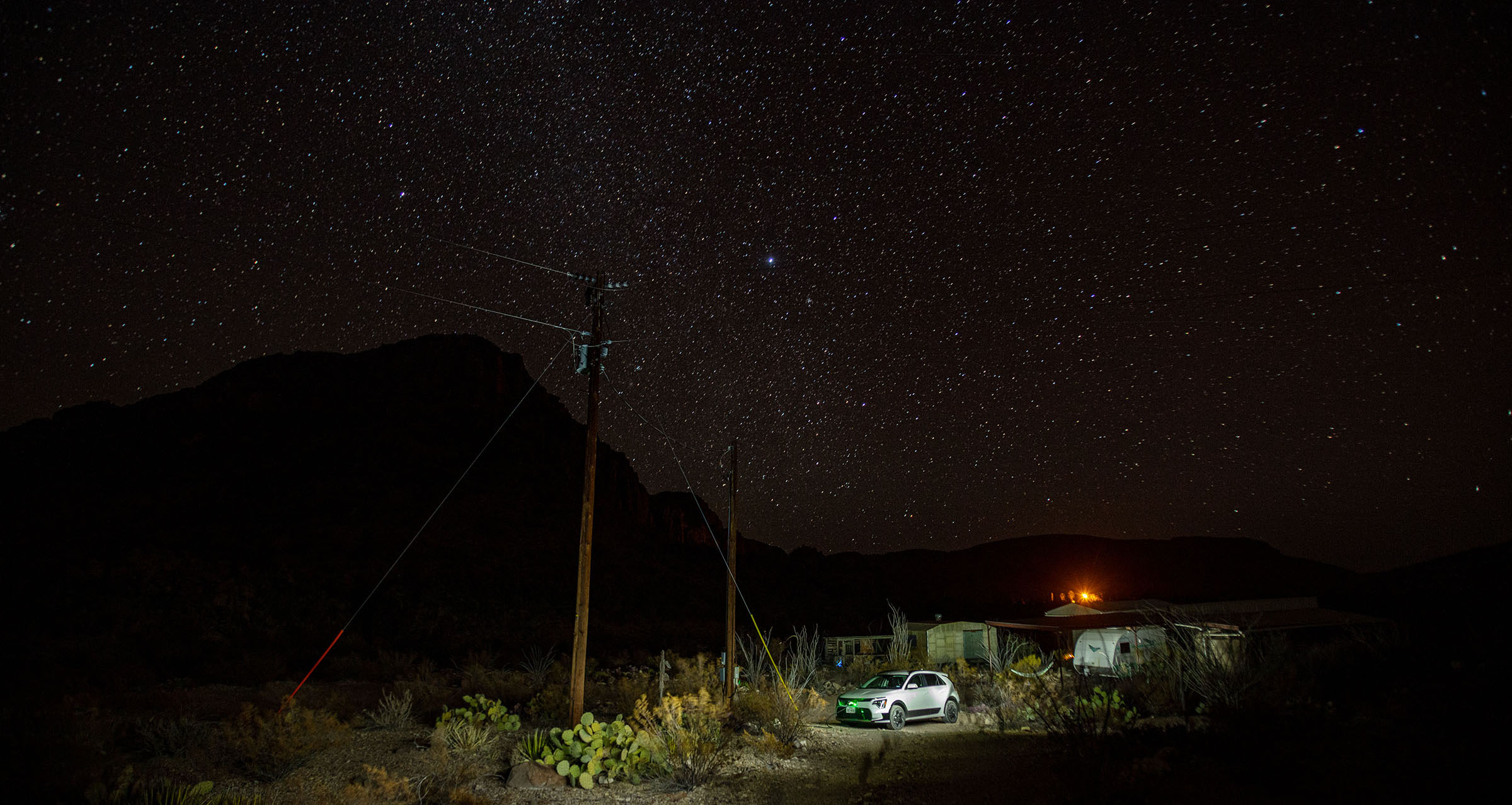 A bright green LED glows at the front of a white vehicle parked under a wide night sky filled with stars