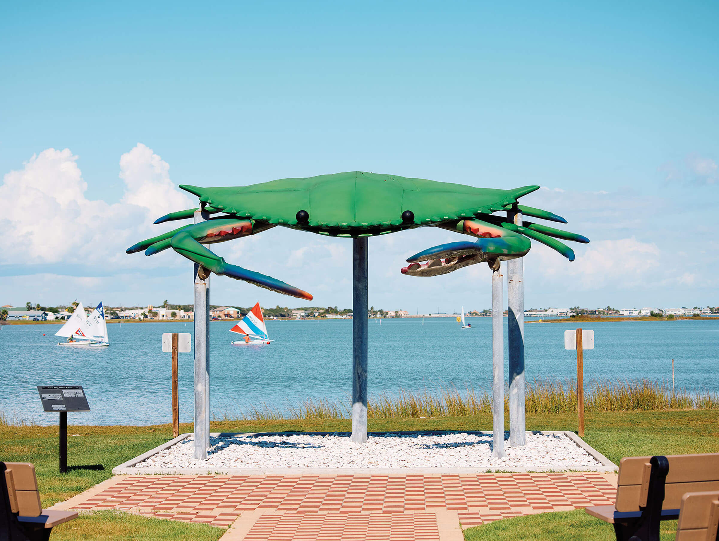 A large green sculpture of a crab in front of a blue sky and water scene
