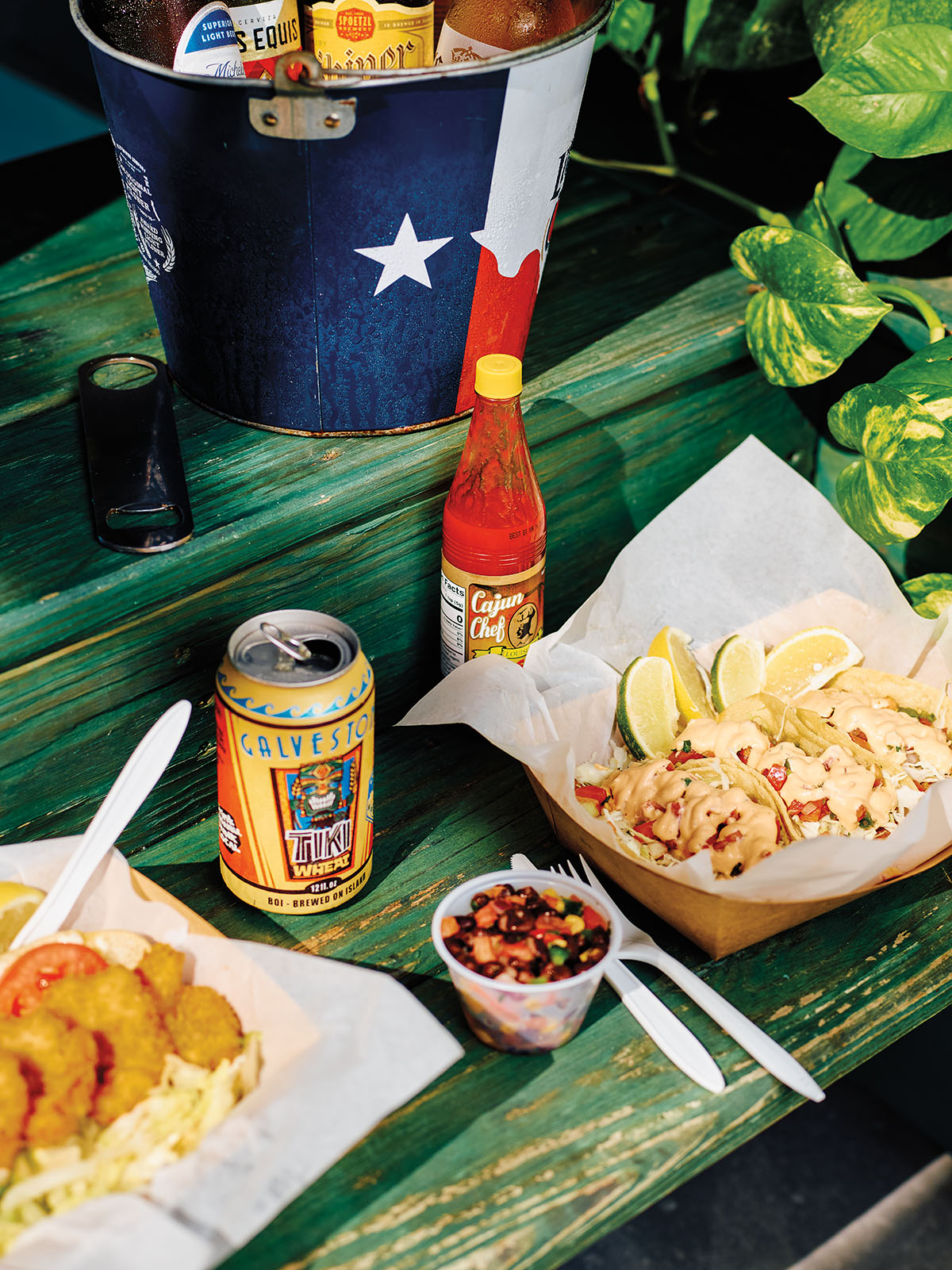 Fish tacos in baskets lined with paper served with a can of beer on a green-stained wooden table