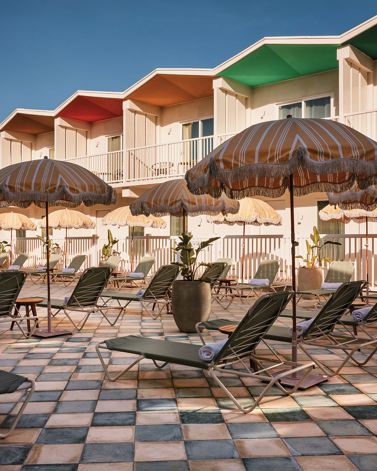 The exterior of a hotel with colorful midcentury styling and umbrella-covered chairs