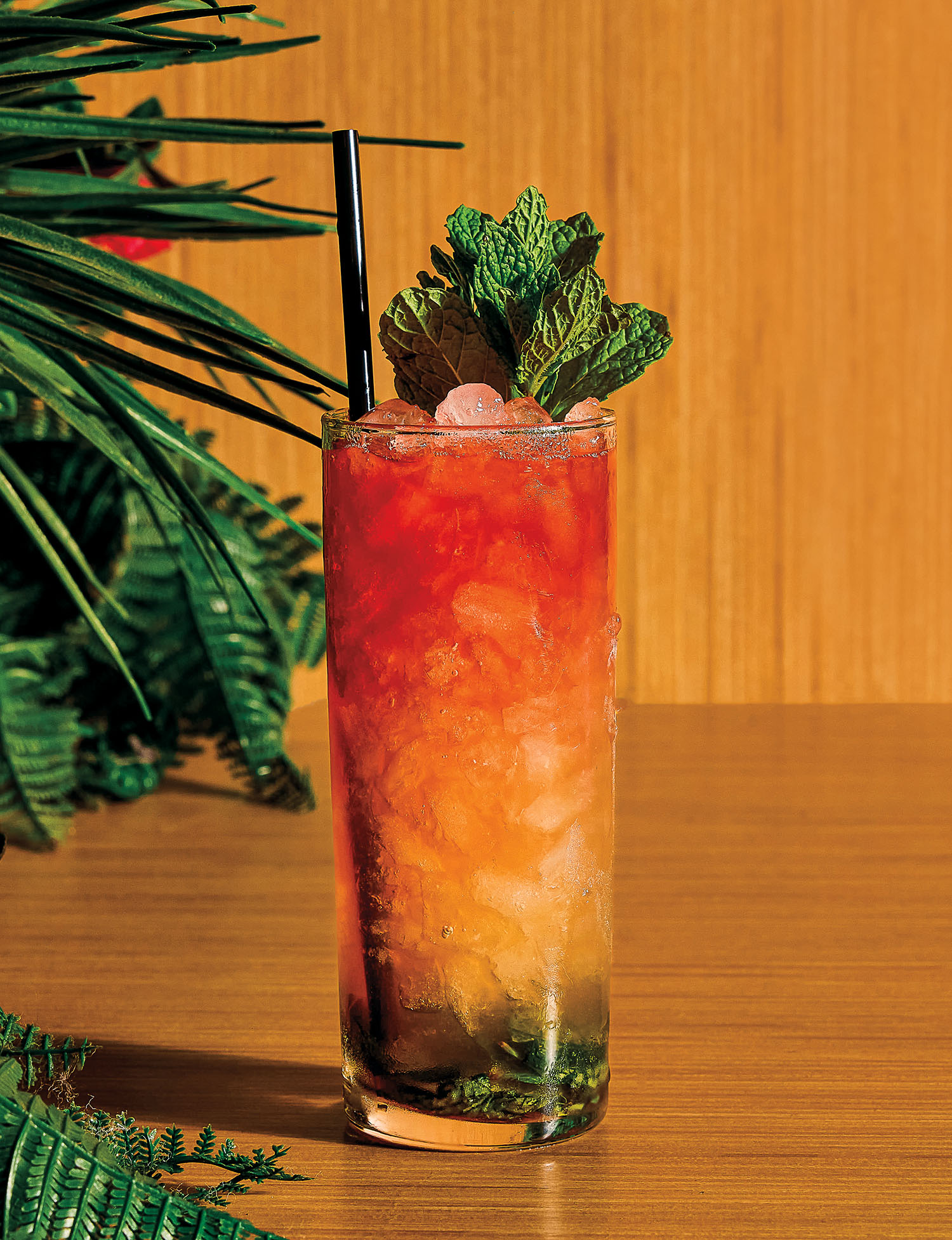 A colorful, red and orange layered cocktail served in a tall glass garnished with mint