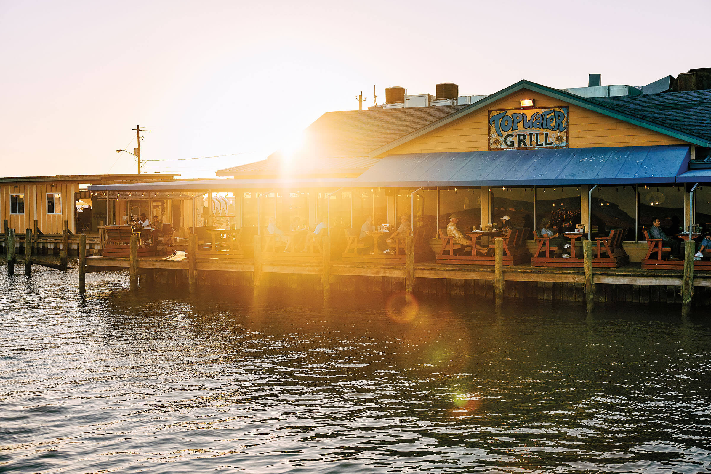 The exterior of a building on a pier on a sunny day above water