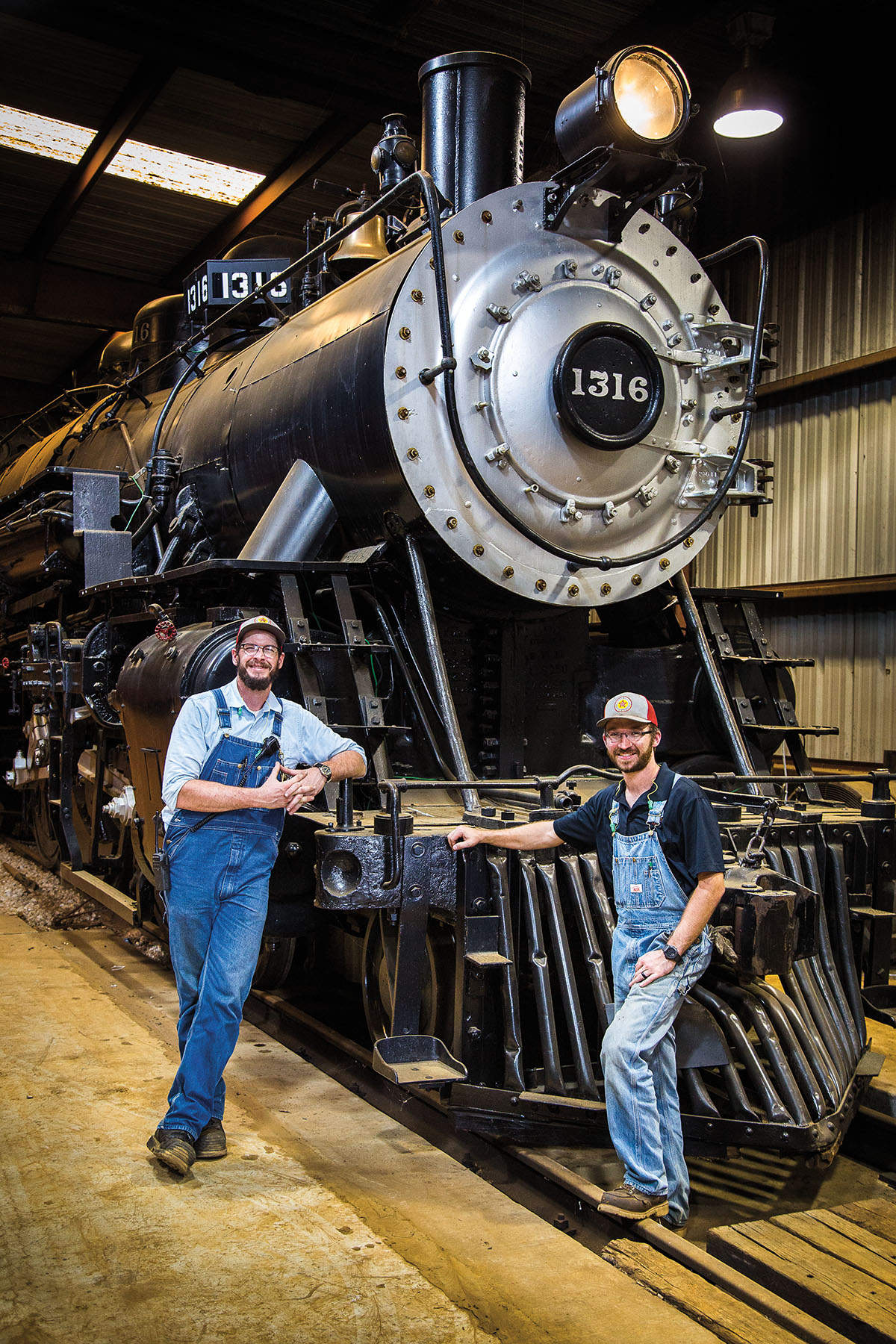 Two men stand in front of a large black locomotive