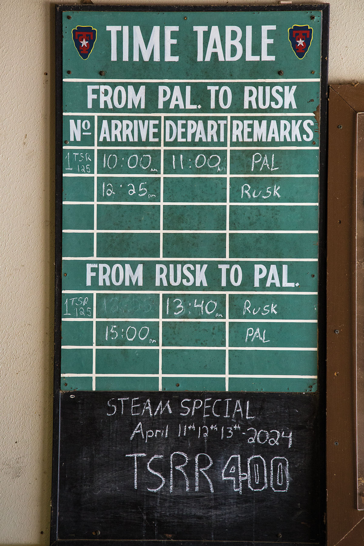 A green chalkboard sign with white lettering reading 'Time Table/From Pal to Rusk'