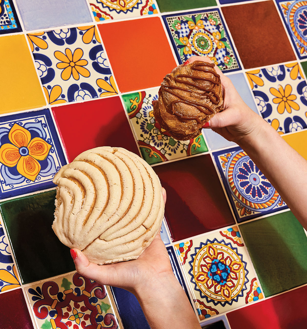 Two hands hold golden pastries in front of a brightly-colored tile background