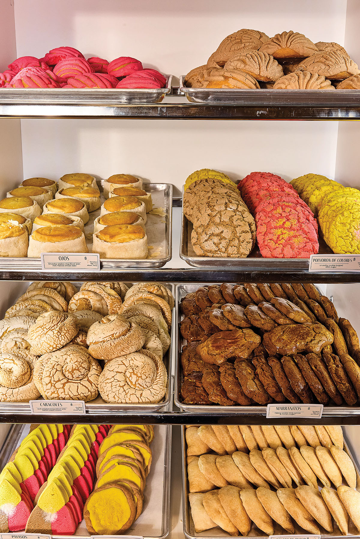 A collection of brightly-colored pastries on silver sheet trays in a bakery case