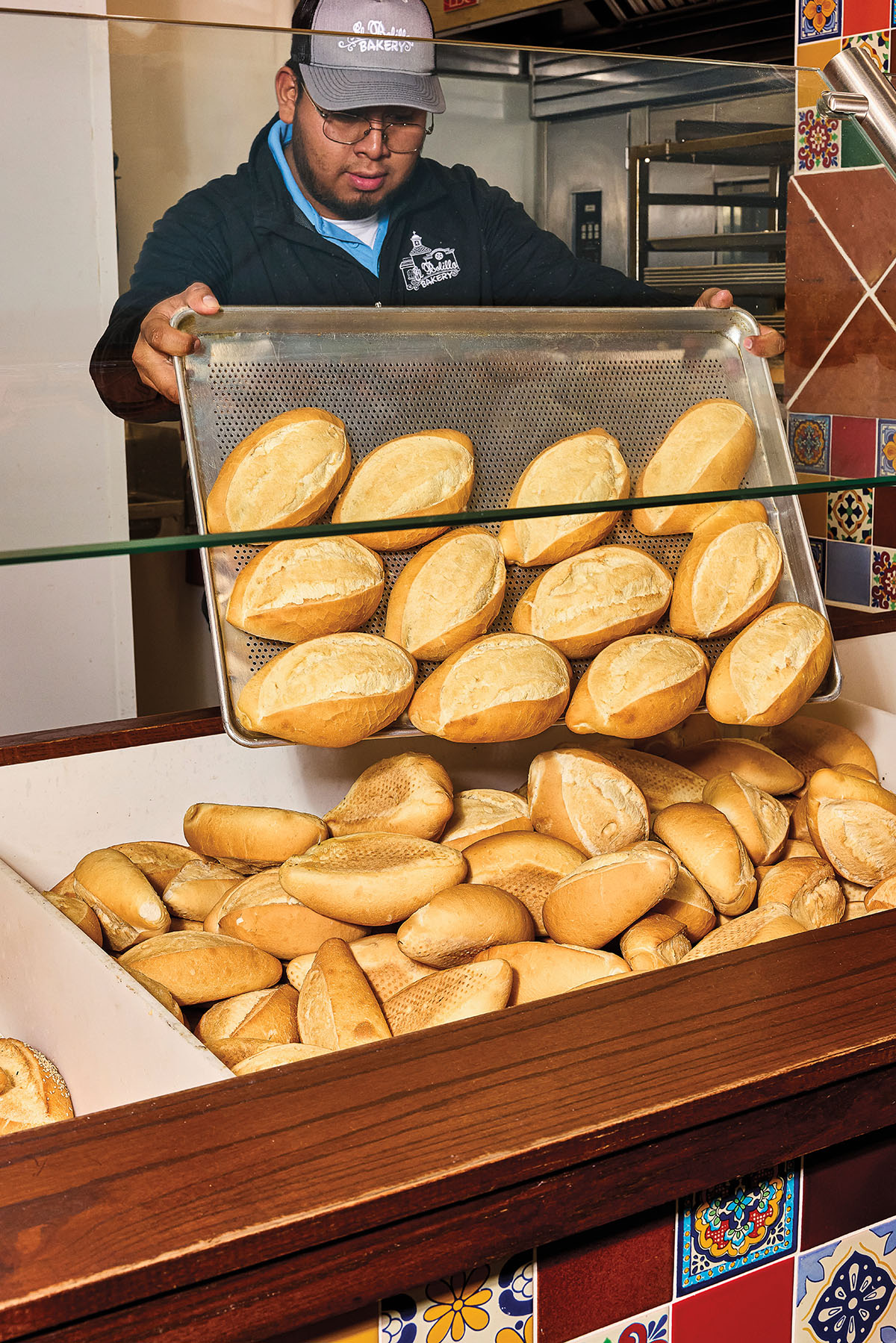 A person holding a large silver pan of breads dumps the bread into a display container