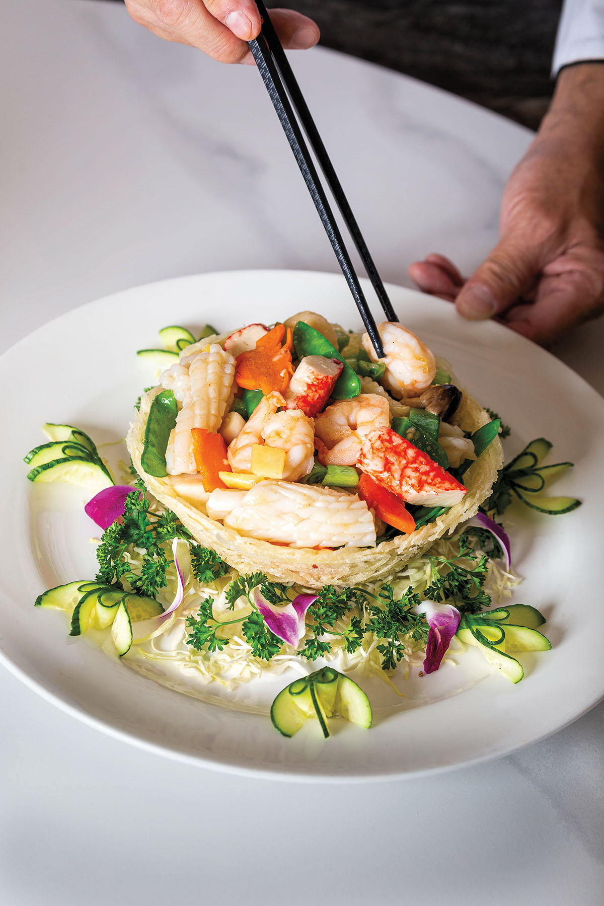 Black chopsticks reach for a piece of pink fish on a plate of vegetables