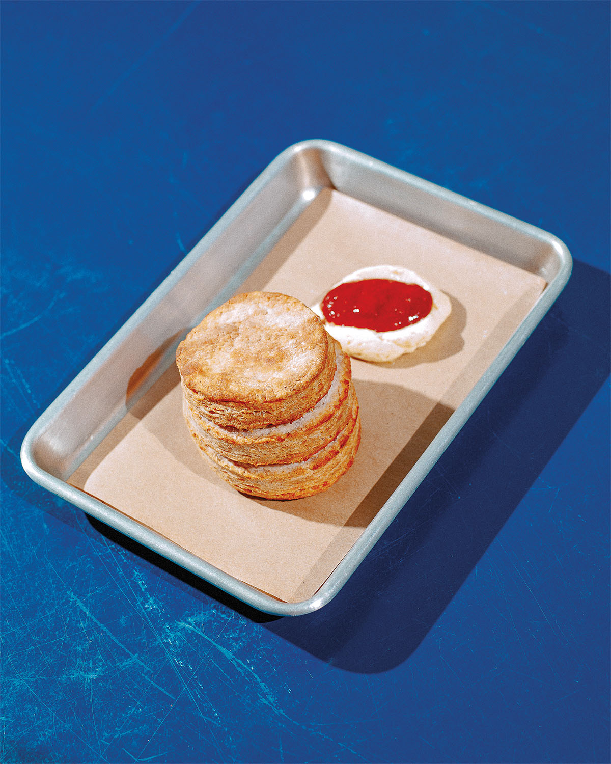 A silver bakery tray with a tall golden biscuit next to a small portion of butter and jam