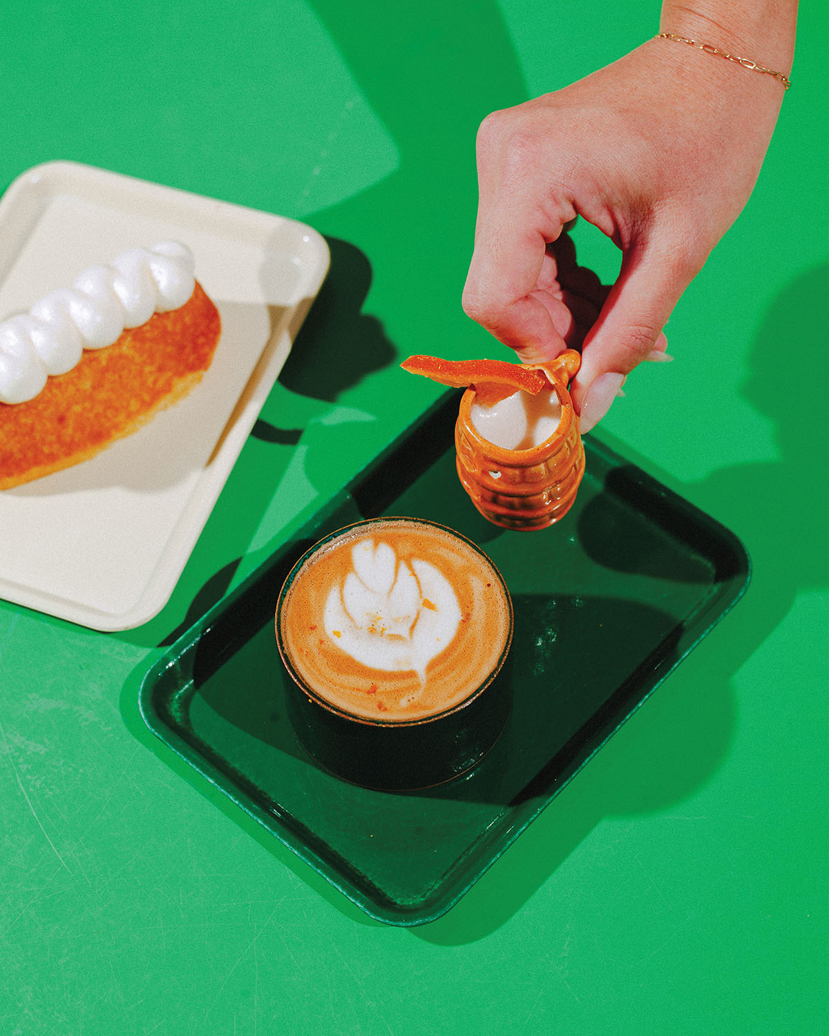 A person's hand reaches down to grab a coffee and small cup of milk from a green tray