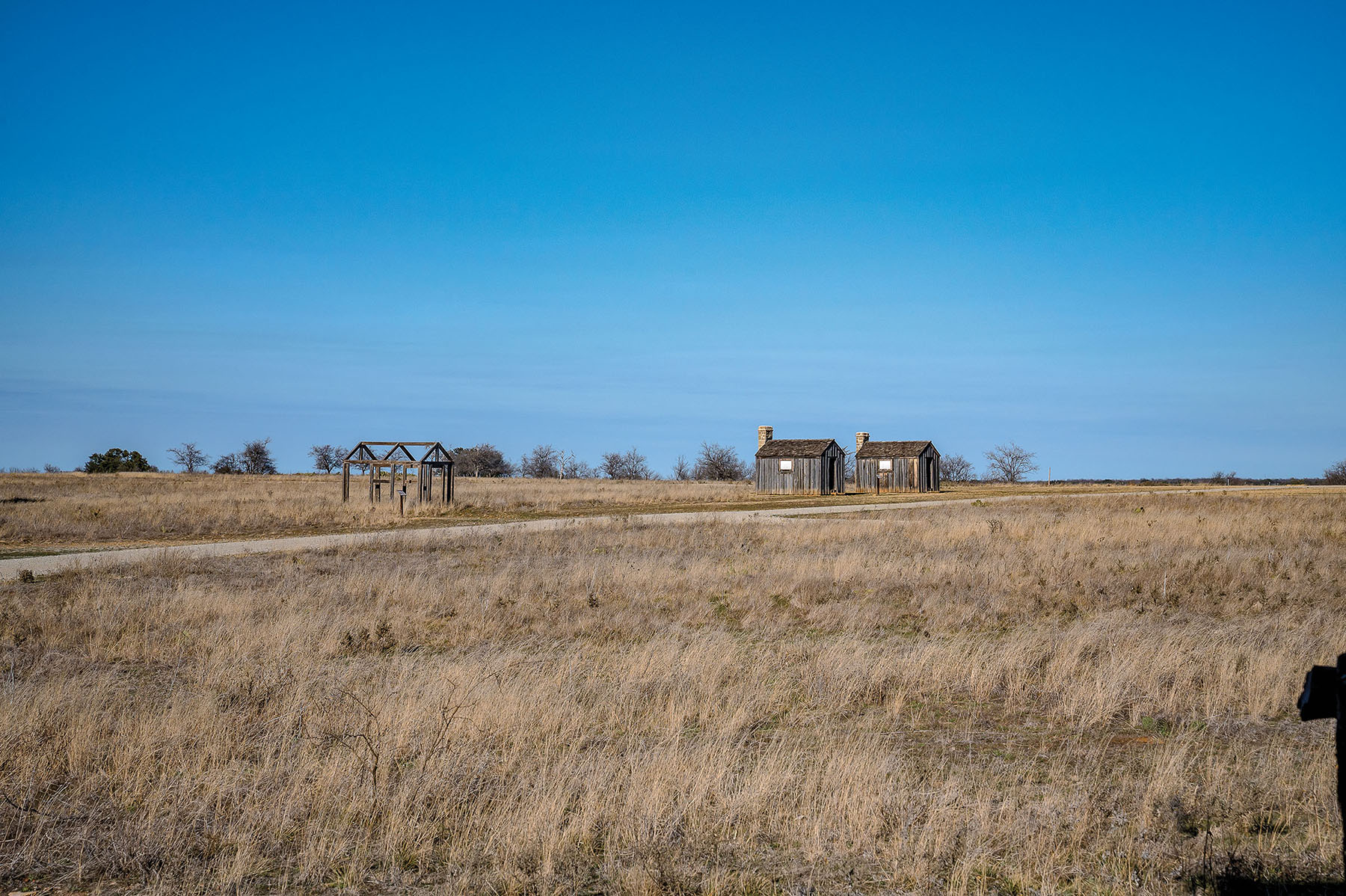 Two small wooden houses on a grassy prairie under blue sky