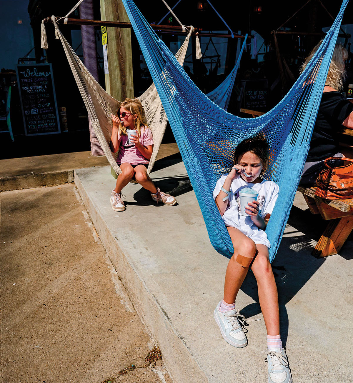 Two young people eat ice cream while sitting in large, colorful netted swings