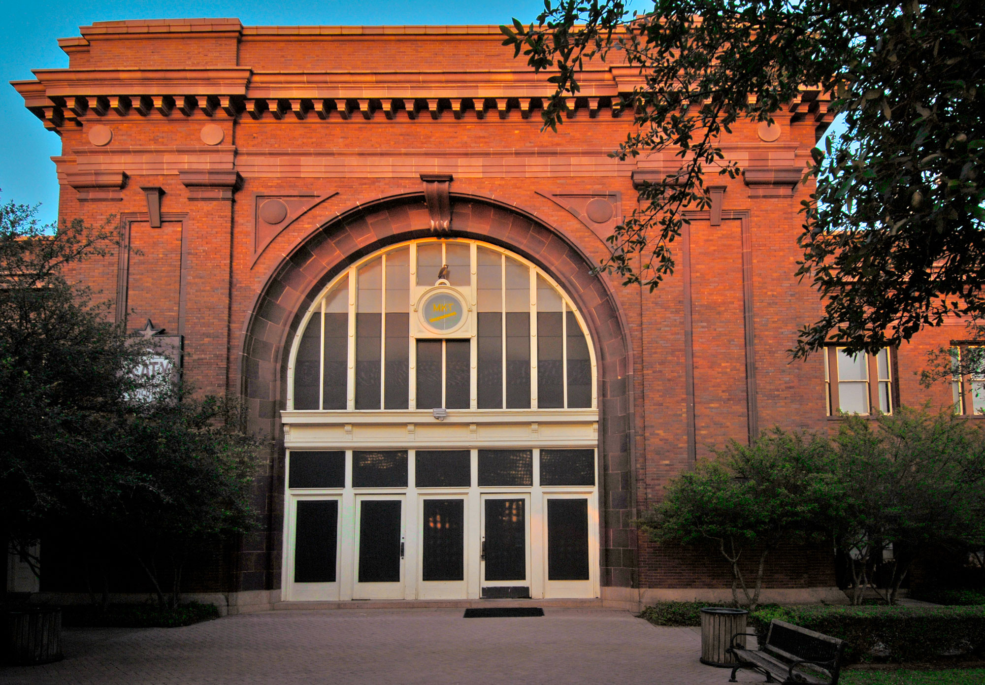 A red brick building with a large, arched window paneled entrance at dusk