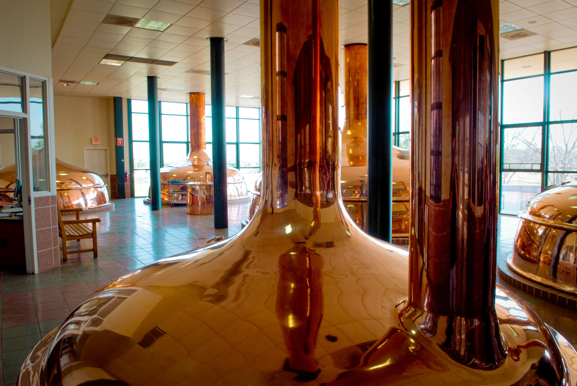 Large, shiny copper floor-to-ceiling vats in a room with windows