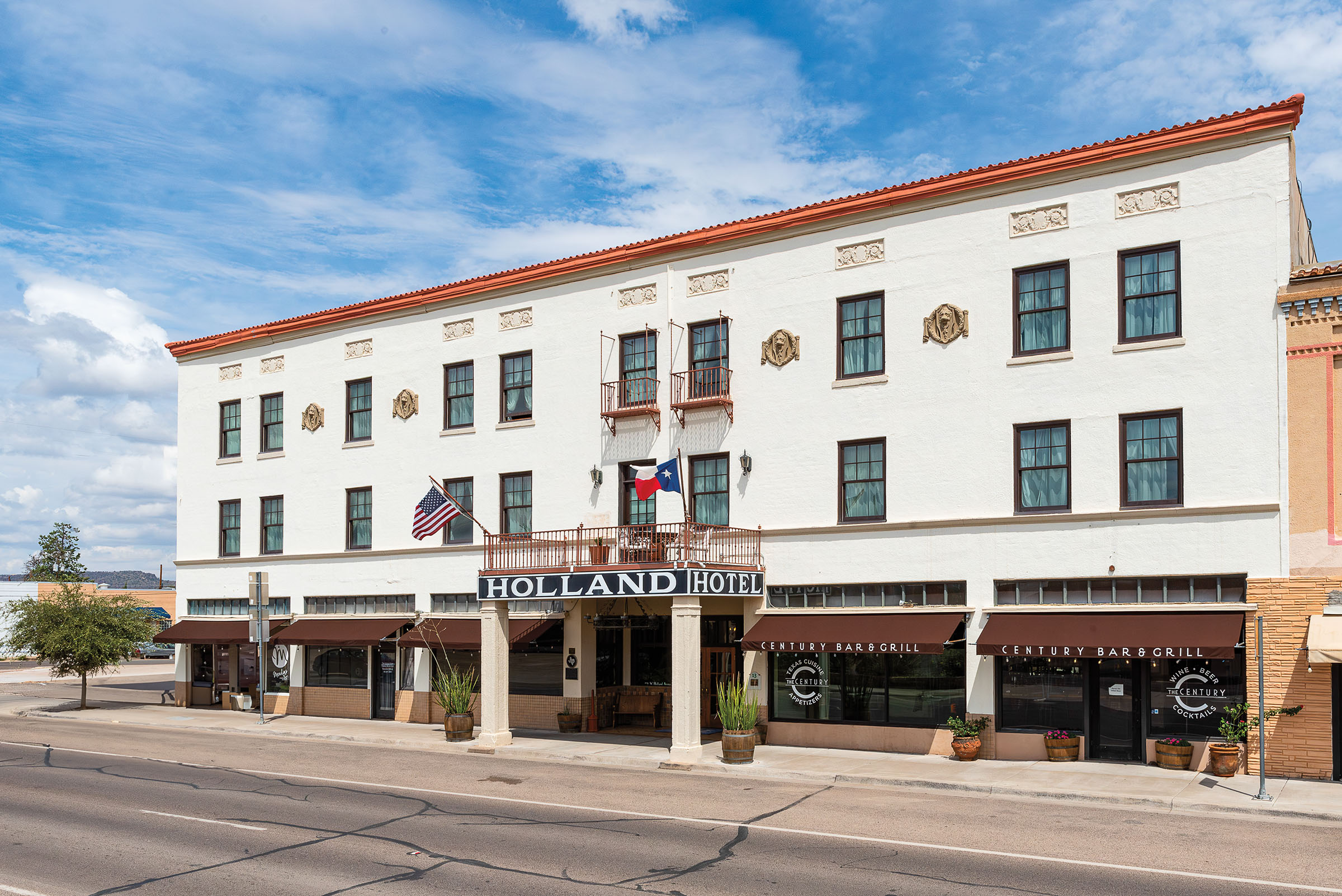 The exterior of a three-story white hotel under blue sky on a city's main street