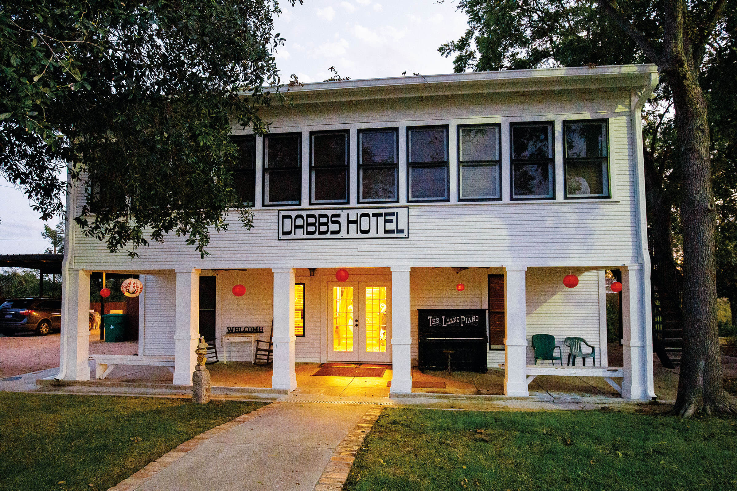 The exterior of a short white hotel beneath green trees. A sign reads "Dabbs Hotel"