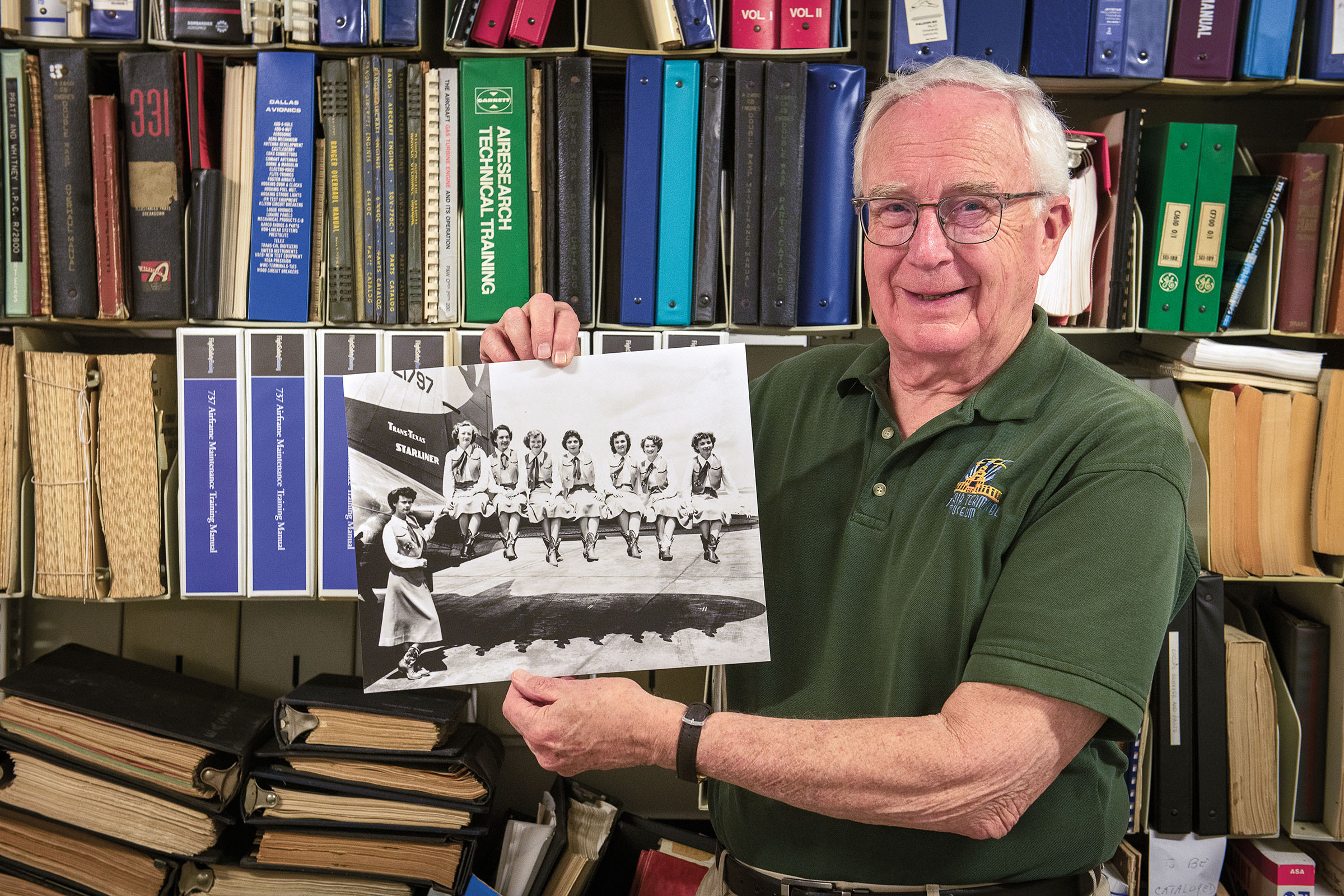 A man holds a black and white photograph in front of a wall of books