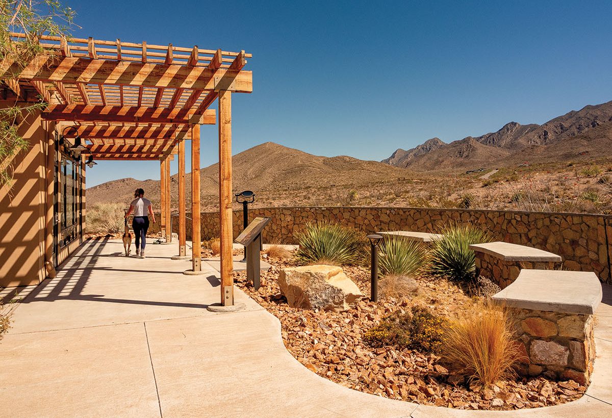 A person walks under a wooden awning with mountains in the backdrop.
