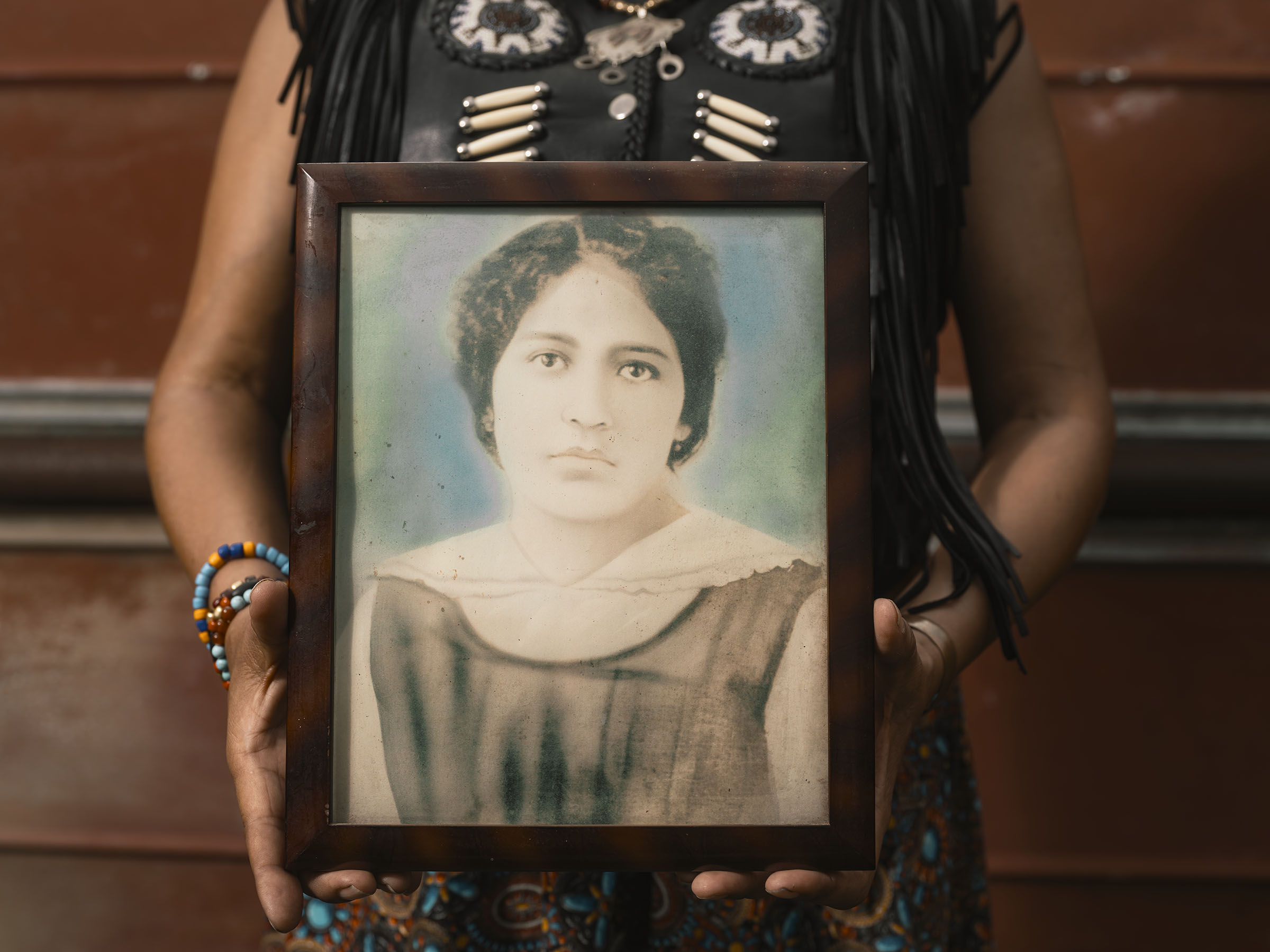 A woman's arms hold a frame with an old washed out portrait of another woman.