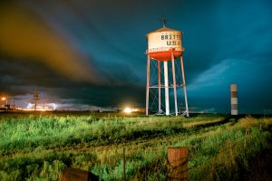 A leaning white and red water tower stands in a field at night. The words "Britten U.S.A" are stamped across the front.
