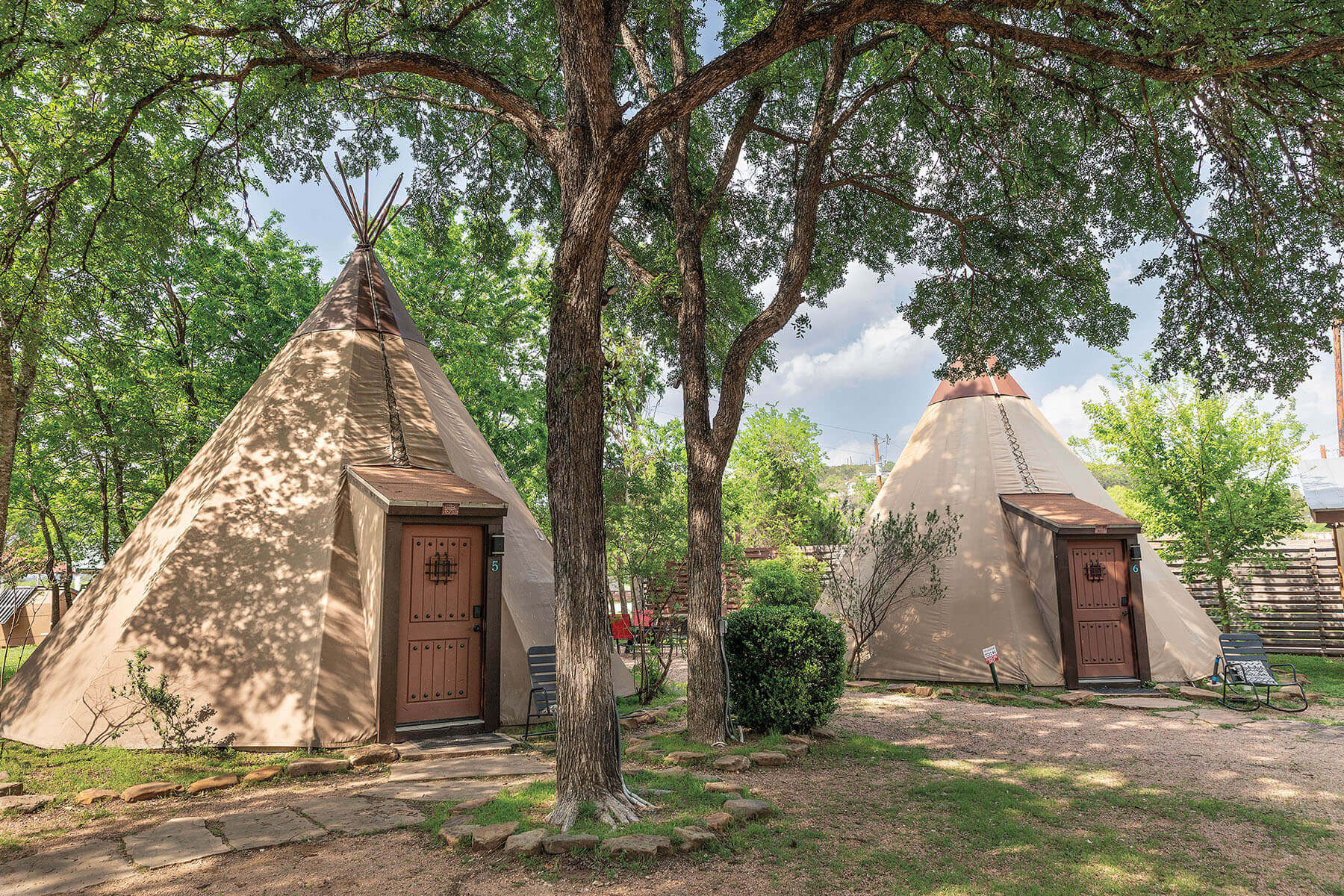 Two tall tan tipis on a dirt embankment next to a river