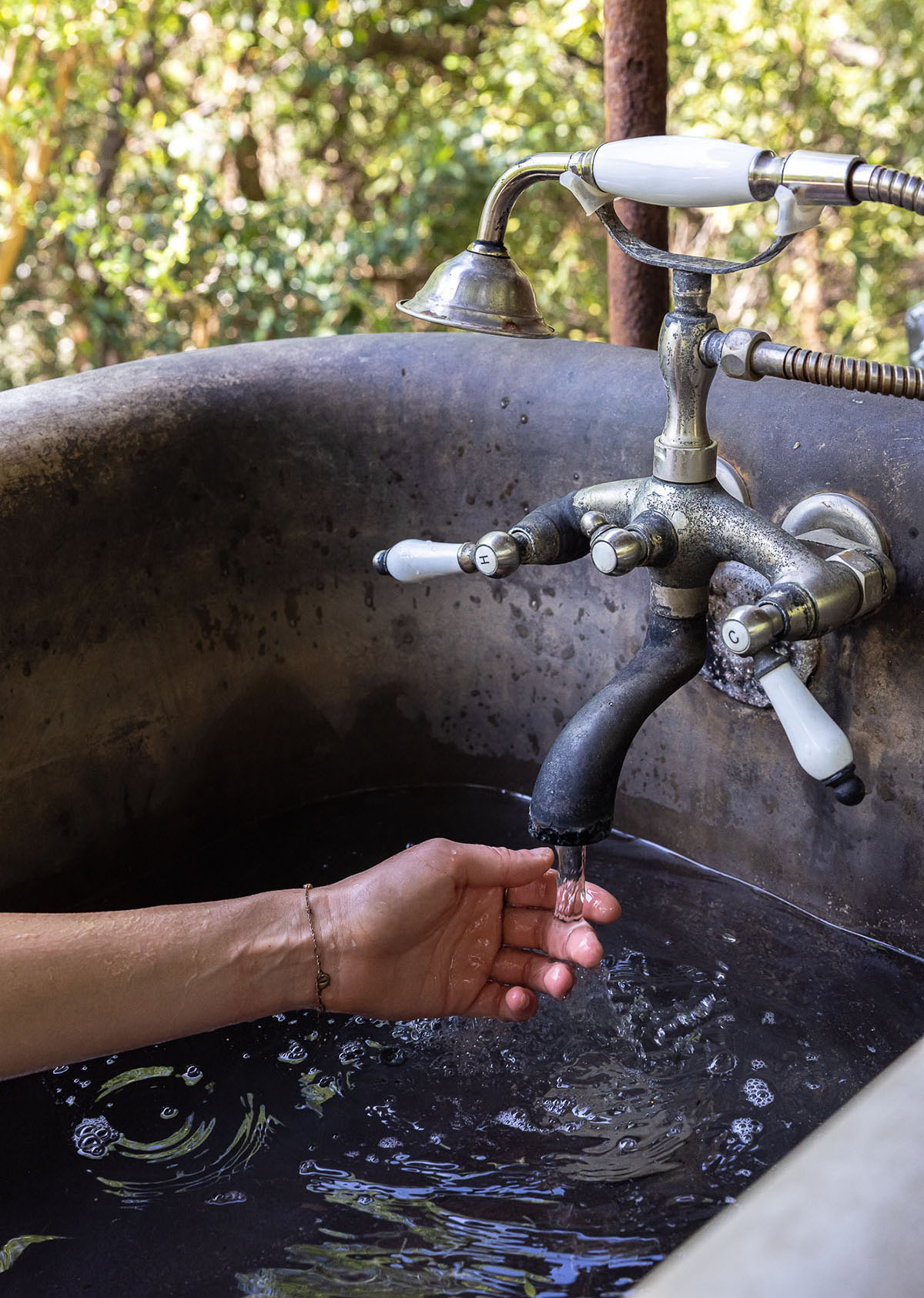 A person's hand reaches out to touch water flowing from a dark metal tap