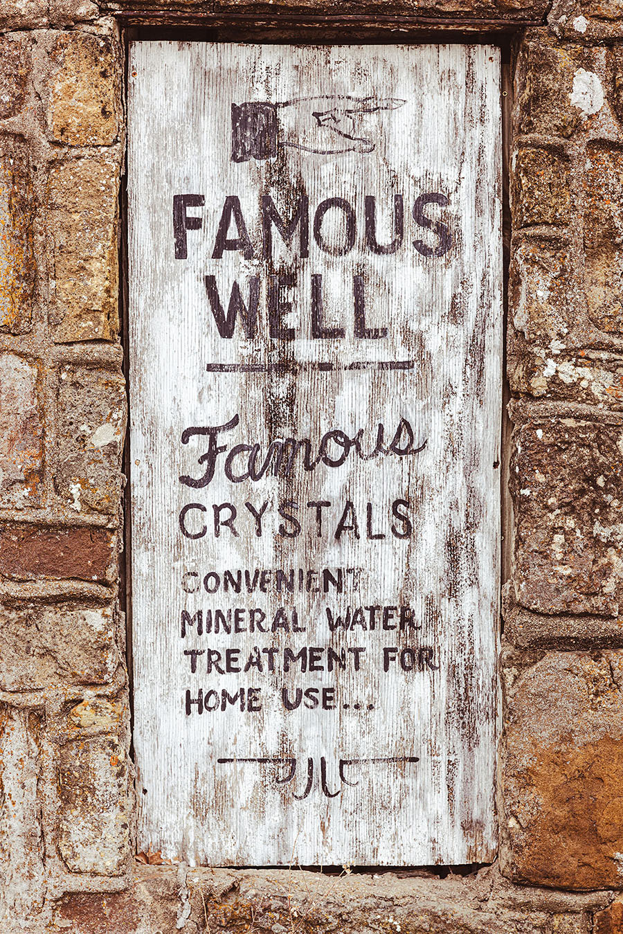 A faded wooden sign reading "Famous Well/Famous crystals/Convenient mineral water treatment for home use"