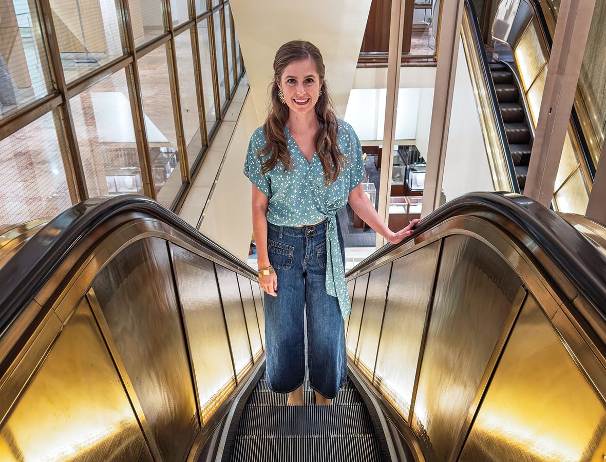 A woman rides up an escalator in a building.