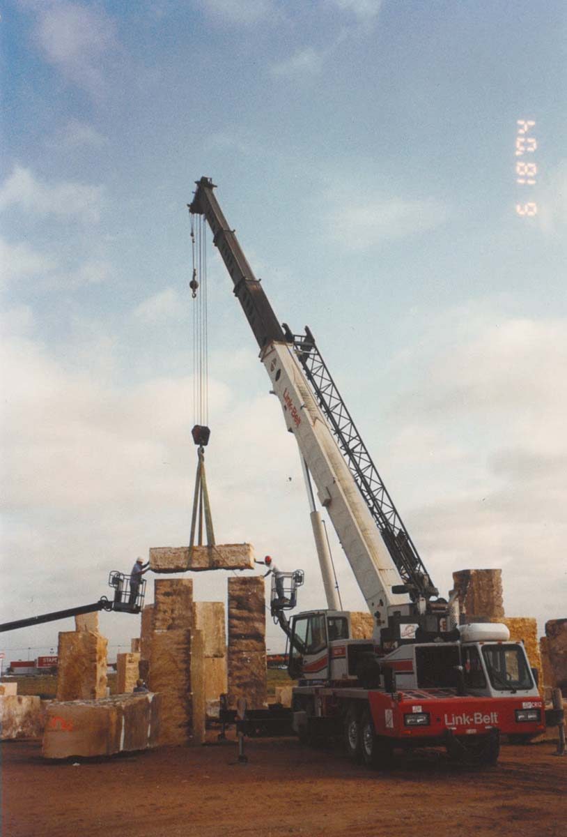 A metal construction crane lifts a piece of white sandstone om front of bright blue skies