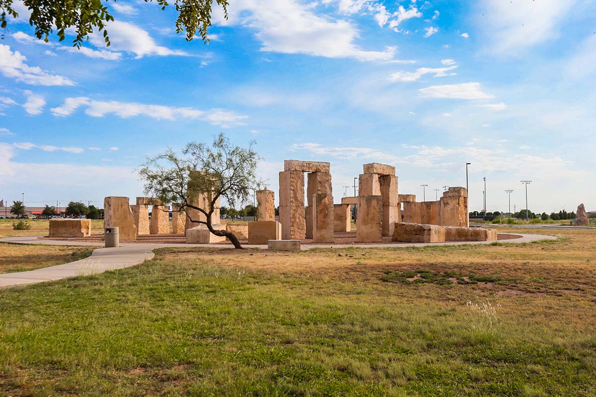 White pieces of limestone are arranged in a circle on a green plot of grass in front of a vibrant blue sky dotted with fluffy clouds