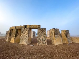 Faded pieces of white limestone are arranged in a circle on brown grass behind a light blue sky