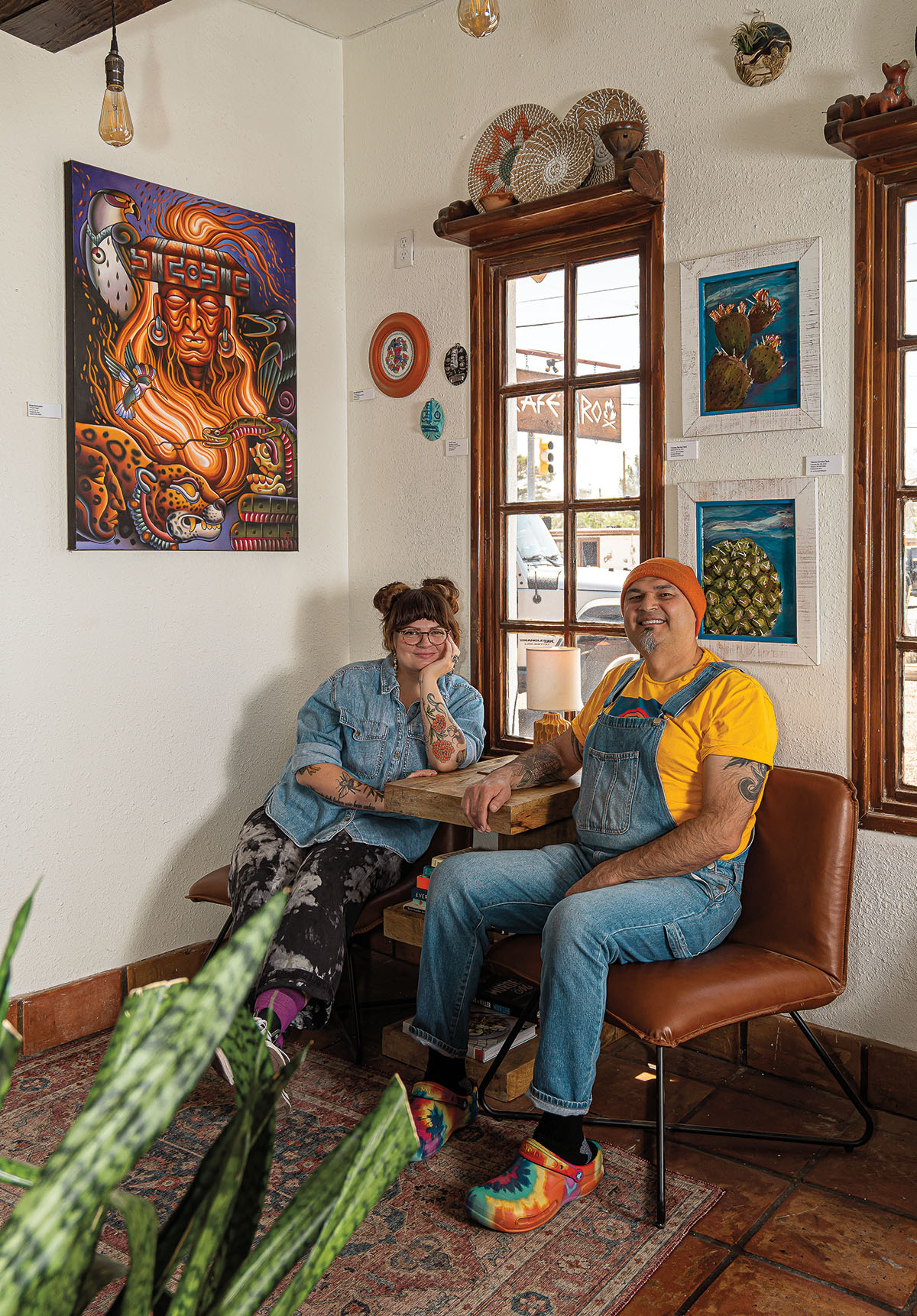 A man and woman sit next to each other in the corner of a room with white walls covered in art.