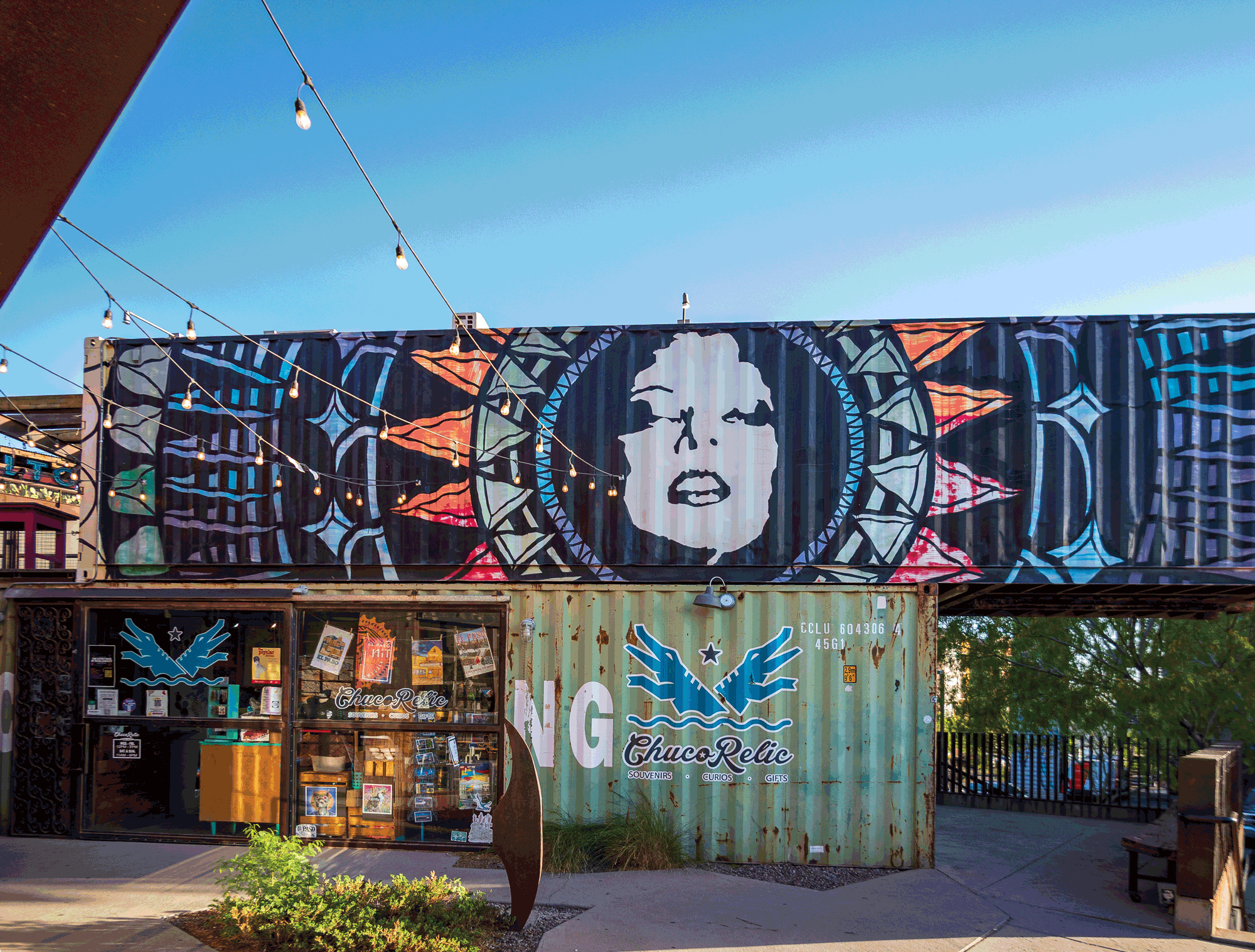 Two shipping containers painted with triangle patterns and a person's face are stacked on top of each other.