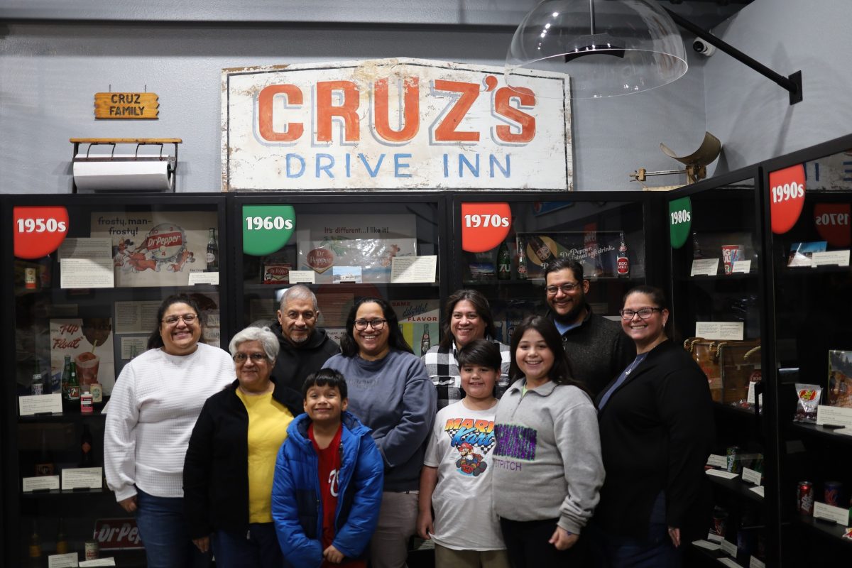 The Cruz Family stands in front of their convenience store sign that reads "Cruz's Drive Inn."