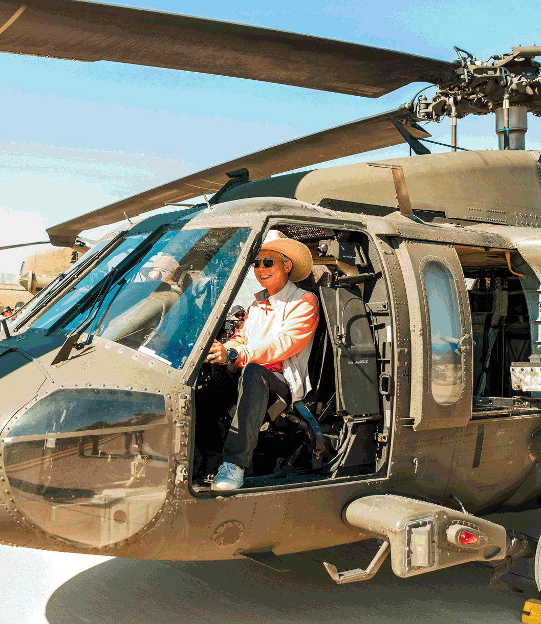 A person wearing a cowboy hat sits in the cockpit of a grounded helicopter.