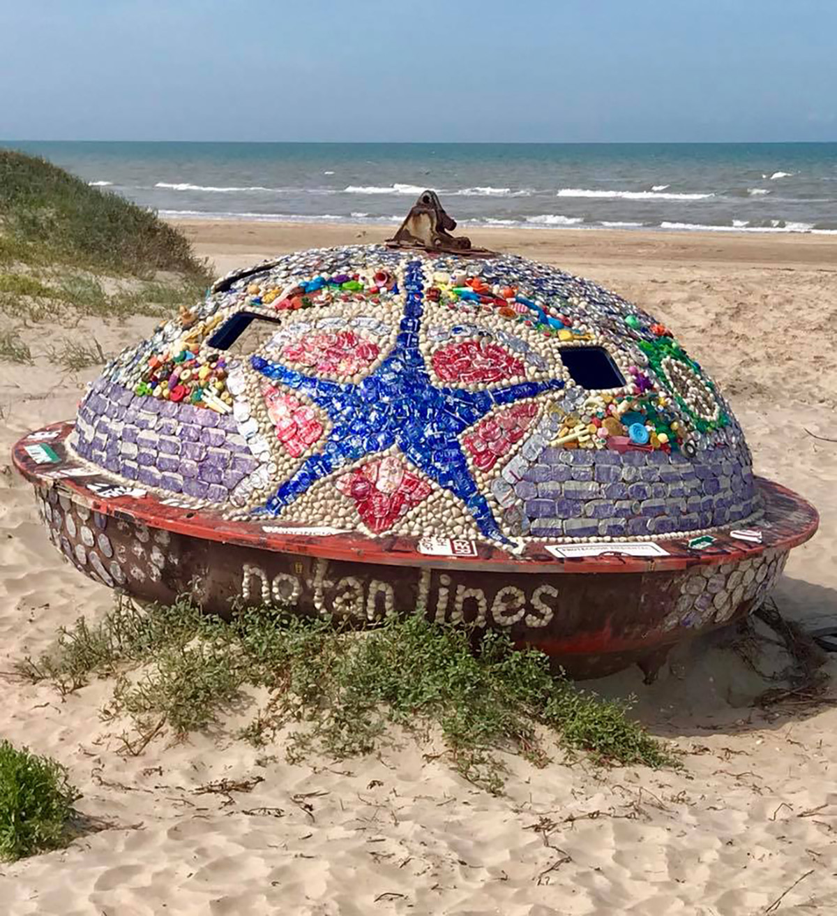Doug Wicks' "UFO" decorated with beer cans and bottle caps. Bottle caps at the bottom of the capsule spell out "no tan lines."