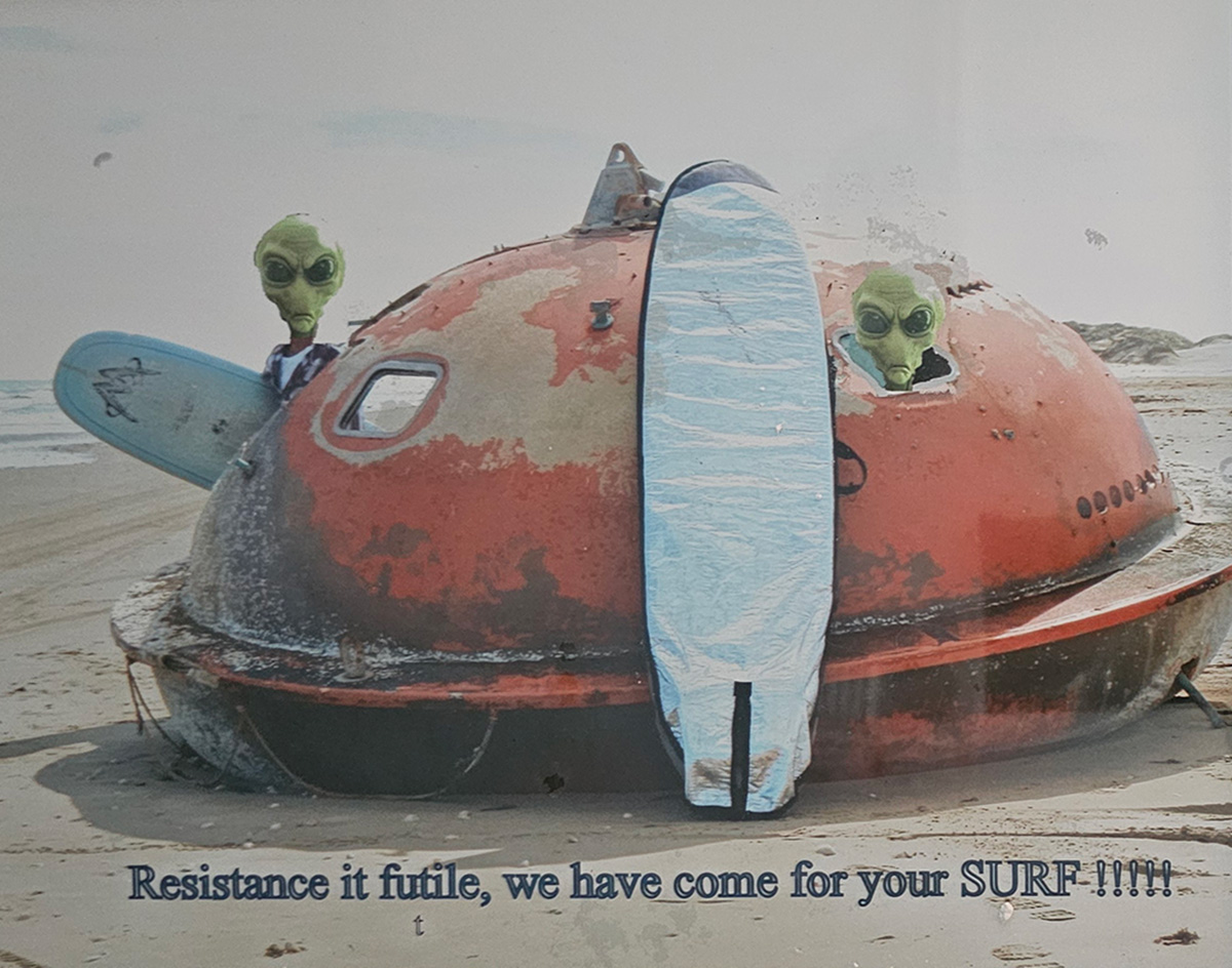 Two people wearing alien masks and holding surfboards pose inside an orange oil rig washed up on the beach. The caption on the photo reads, "resistance is futile, we have come for your surf!!!!!"