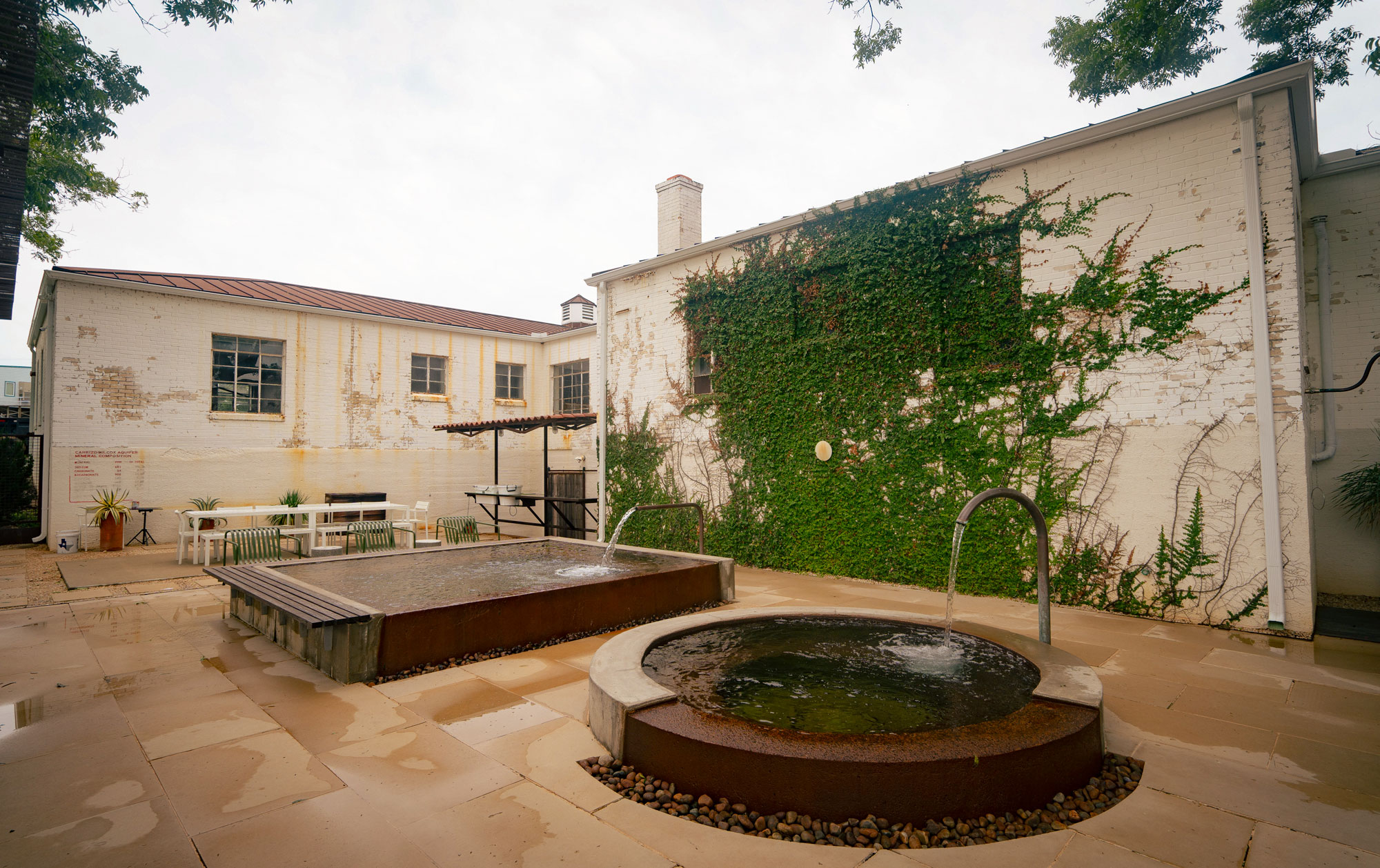 Water runs out of spouts into two small soaking pools in the courtyard of a historic building covered in vines.