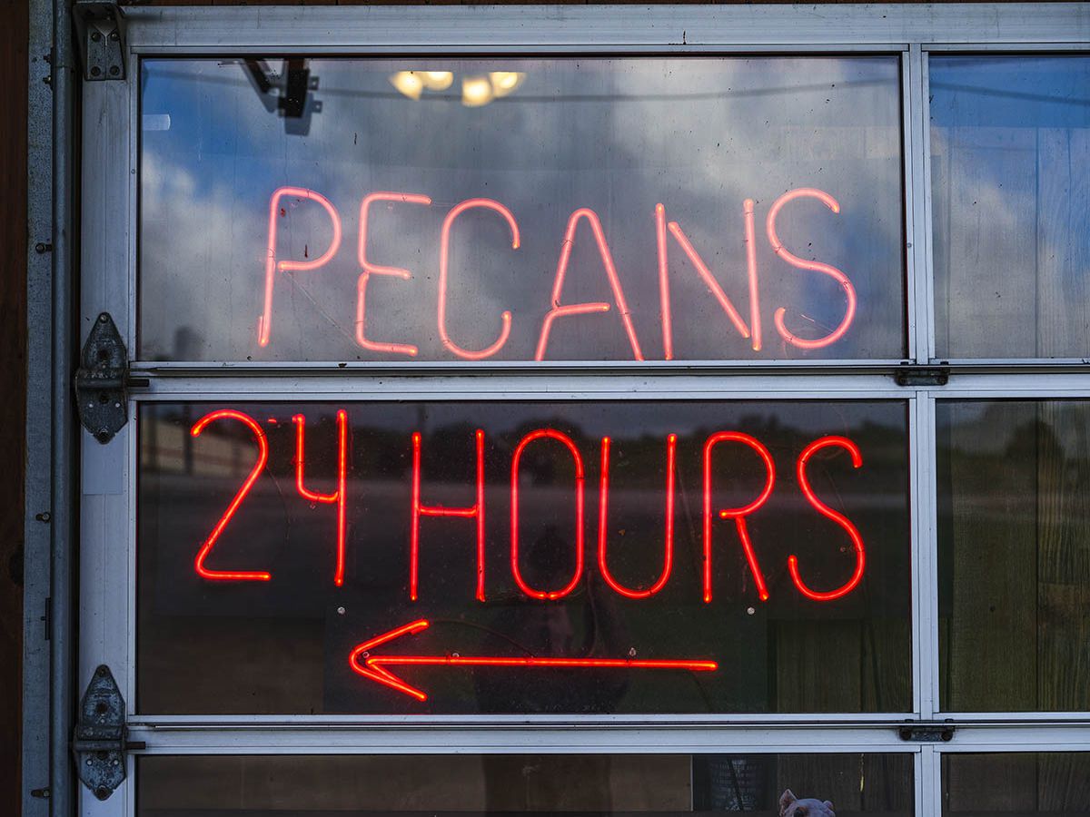 a red neon sign reading "pecans 24 hours" above an arrow