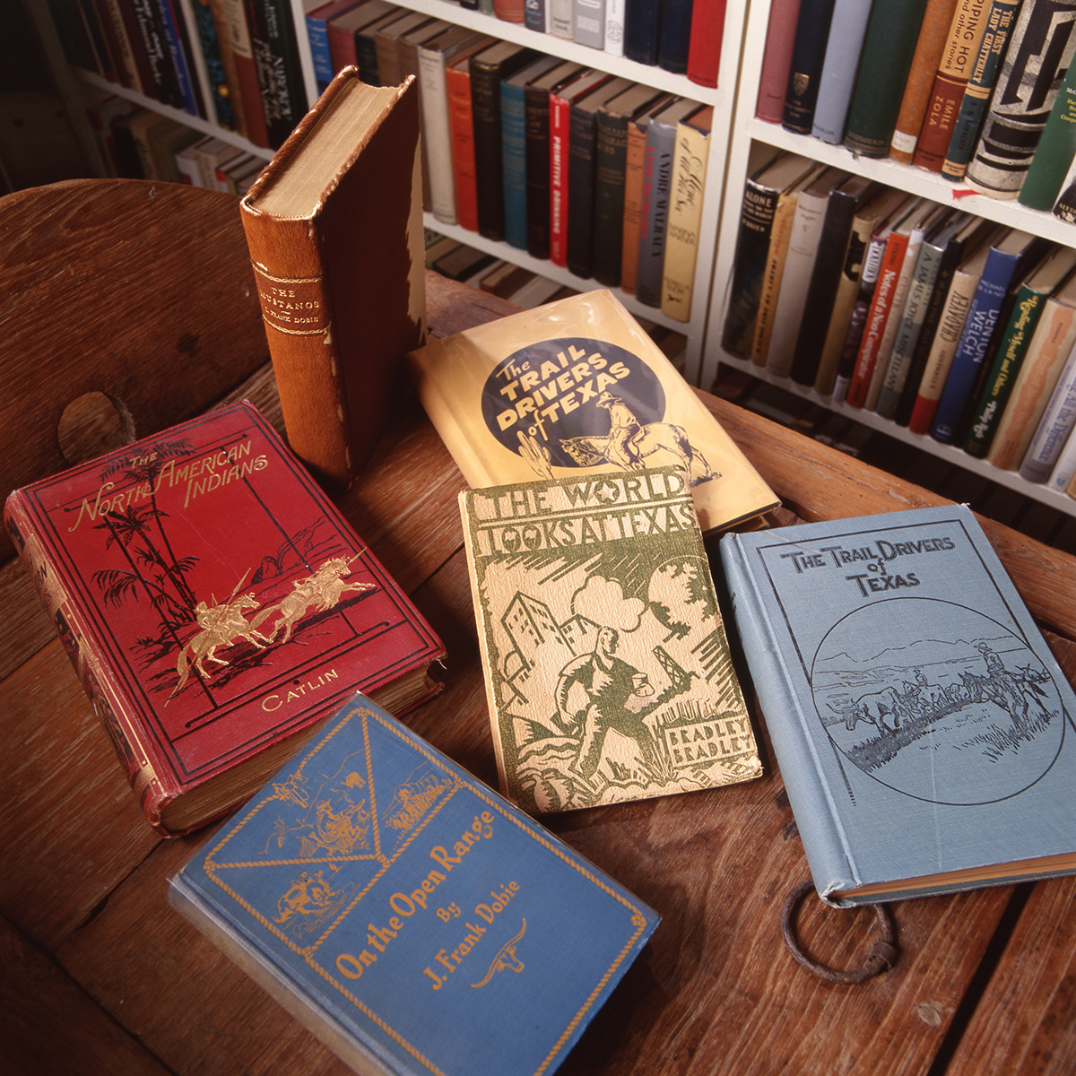 Six vintage books with red, orange, yellow and blue covers sit on a dark brown wooden table