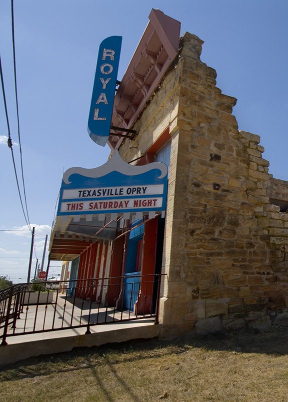 A white brick theatre with a cerulean marquee vertical sign reading "royal."
