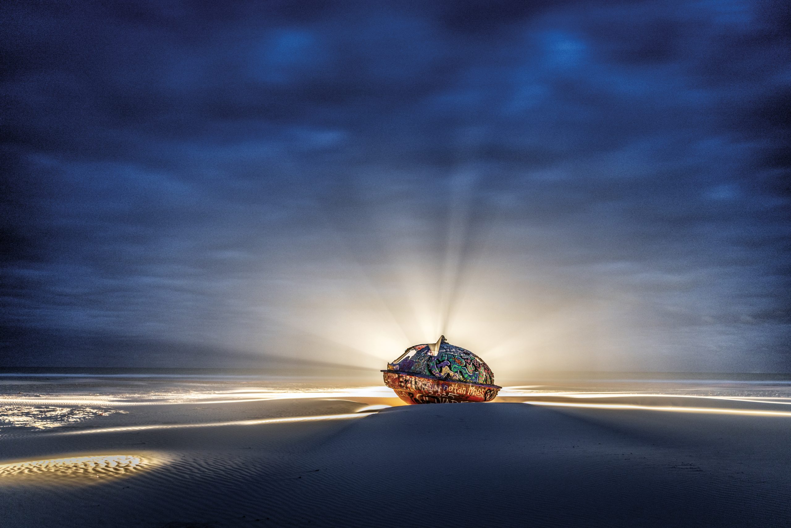 A UFO-shaped object sits on a beach backlit by a descending sun