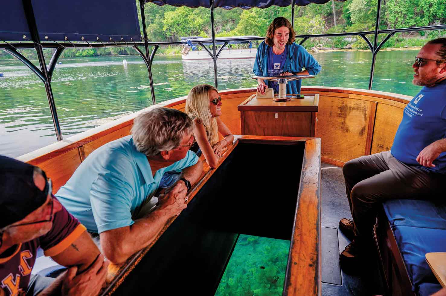 People peer down into the glass bottom of a boat on a river