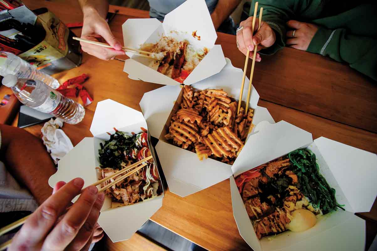 Hands holding chopsticks pick at different white cartons of food