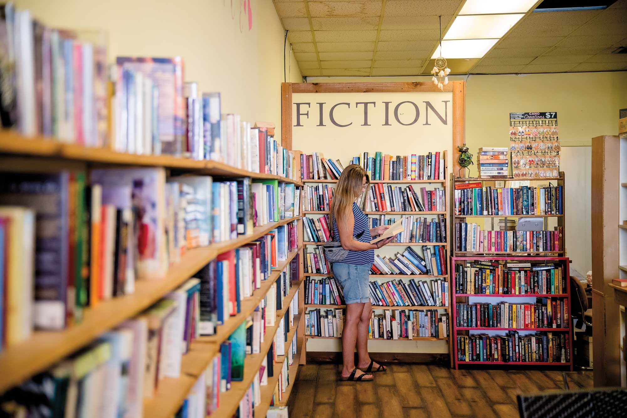 A person reading a book in a bookstore with a sign that reads Fiction behind them