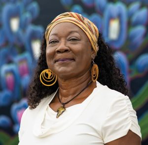 A smiling woman wearing a headband and earings and a white shirt