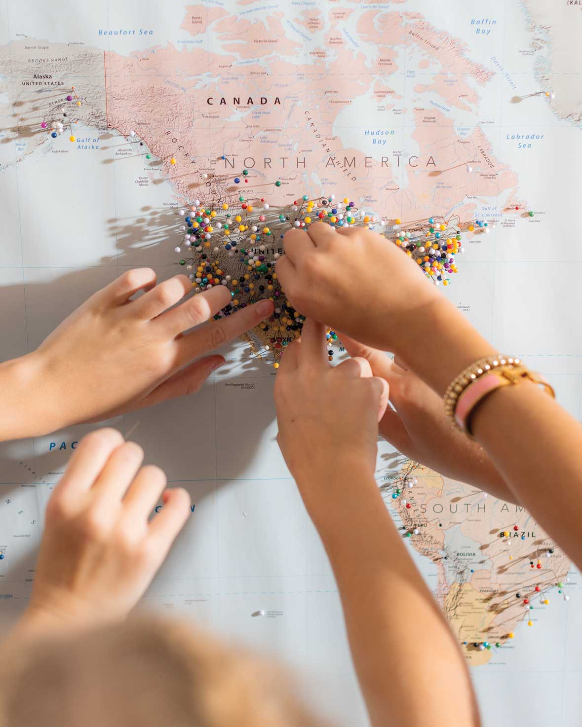 Hands press pins into a paper map of the USA.